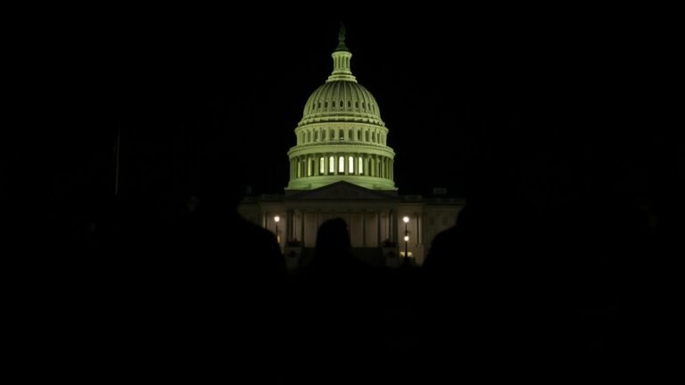 US Capitol building at night with silhouetted figures.