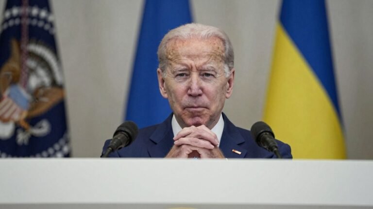 Biden official looking serious, Ukraine flag background.